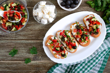 Classic bruschetta with tomatoes and feta on a white plate on a wooden background. Italian sandwiches with toasted baguette, goat cheese, fresh vegetables, basil. Top view, flat lay.