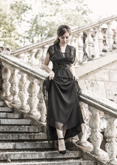 Fototapeta na wymiar Beautiful girl in a black evening dress on the steps of an abandoned palace. Pretty woman with scars. Young girl in retro style. girl steps up the stairs. Pretty Woman