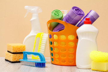 Bottles of dishwashing liquid, basket with garbage bags and sponges on wooden desk.