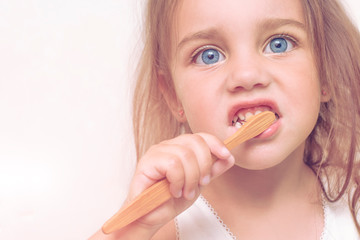 Child girl 3 years old brushes her teeth with a bamboo toothbrush. A beautiful child with big blue eyes saves the planet from plastic, the concept of zero waste.