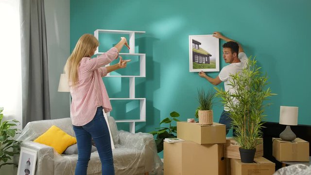 Young couple hangs wall paintings in a new apartment