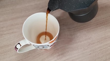 Using italian coffee maker cafetiera in slow motion. Closeup of coffee cup on wooden table. Pouring hot black coffee into white cup with colorful donuts from moka pot in slowmotion. - Powered by Adobe