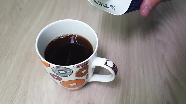 Male hands pour milk from the plastic packaging. Making bubles with milk. Mixing black coffee and white milk. Pouring milk into cup full of coffee in slowmotion on wooden table.