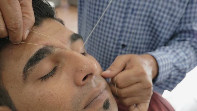 Threading, epilation technique, ancient Asian method of eyebrows hair removing. Beautician makes threading hair removal procedure. Removing hairs from face with thread in beauty salon