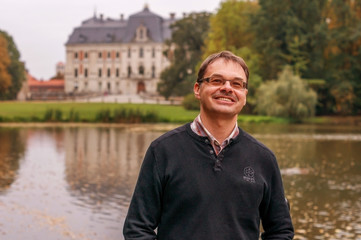 Smiling middle-aged man in the Park in the autumn on the background of the lake and the ancient Palace in Europe.