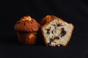 Muffins with raisins and one muffin cut in half on black background