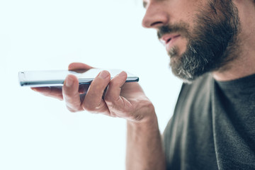 close-up of bearded caucasian man recording voice message or using voice assistant on mobile phone