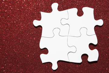 Overhead view of white jigsaw puzzle on red glitter background