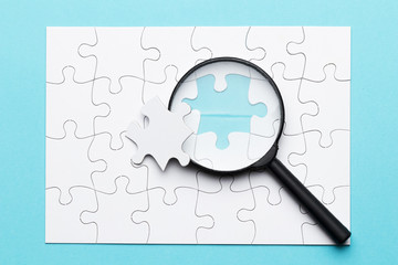 Magnifying glass and missing puzzle piece on white grid puzzle on blue surface