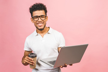 Using laptop. Portrait of handsome casual african american young man drinking coffee while holding laptop computer isolated against pink background. - Powered by Adobe