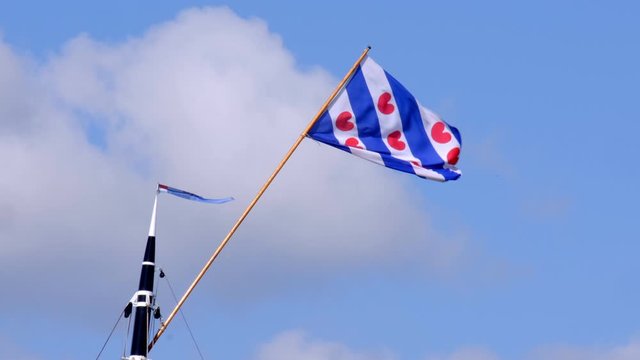 Frisian flag in top of a mast of a classic sailboat during a windy day in summer.