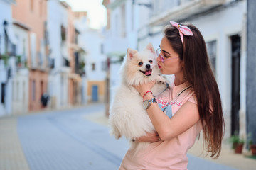 Portrait of a young girl kissing her white fluffy pomeranian dog.