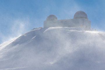 Fototapeta na wymiar A mountain station with domes in the Spanish winter sports area Pradollano high in the Sierra Nevada. The strong wind causes considerable snowdrifts in the air.