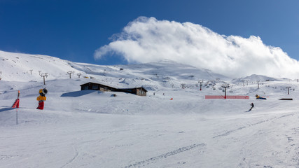 In the Spanish winter sports area Pradollano high in the Sierra Nevada. Snowboarders are on the slopes and you can see chairlifts. Blue sky and snowdrifts.