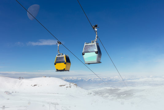 In the Spanish winter sports area Pradollano high in the Sierra Nevada. Cable car cabins in front of blue sky and snowdrifts in the air.