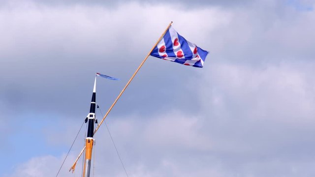 Frisian flag in top of a mast of a classic sailboat during a windy day in summer.