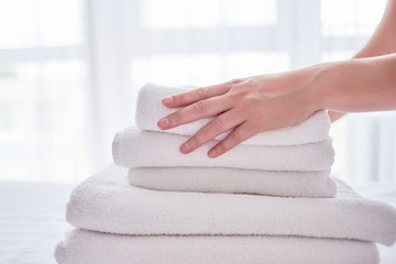 Obraz na płótnie Canvas Woman putting stack of fresh white bath clean towels on bed sheet, copy space. Close up hands of hotel maid with towels. Room service