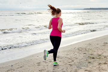 Back view of athletic woman running on sea beach, copy space. Female runner working out at summer morning, full length body portrait. Healthy lifestyle concept