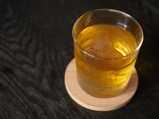 One glas of whiskey on wooden coaster on black table