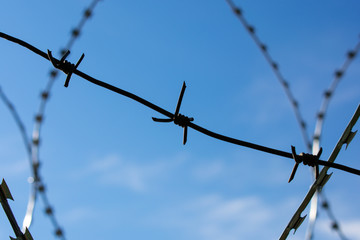 Barbed, rough, wavy wire against a bright blue sky with clouds. Restricted area. Protective wire. Egoza.