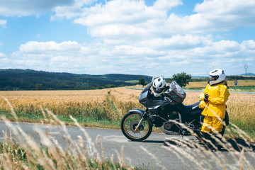 Obraz premium The driver girl in the helmet is wearing a raincoat. Adventure motorbike with side bags. a motorcycle tour journey. Outdoor. World travel on two wheels, freedom concept. field and sky on background