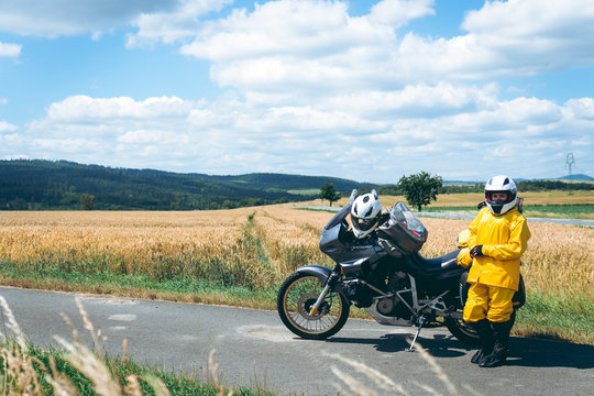 The driver girl in the helmet is wearing a raincoat. Adventure motorbike with side bags. a motorcycle tour journey. Outdoor. World travel on two wheels, freedom concept. field and sky on background