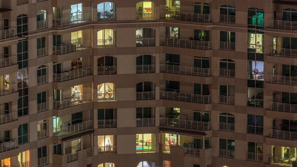Windows of the multi-storey building with lighting inside and moving people in apartments timelapse.