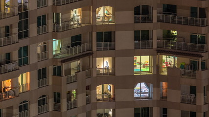Windows of the multi-storey building with lighting inside and moving people in apartments timelapse.