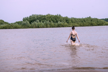 On a warm summer day, the girl goes into the river to swim, copy space, instagram.