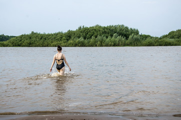 On a warm summer day, the girl goes into the river to swim, copy space.