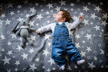 The child lies on a star blanket. Cute newborn baby girl lying in bed. Owl child sleeping on a blue...