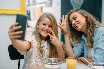 young girl taking picture while having breakfast with her mother at home