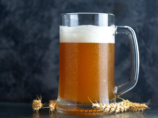 A mug of unfiltered wheat beer on a dark concrete background and ears of wheat