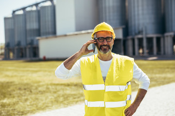 worker in protective wear suing cellphone in front of grain silos © cherryandbees
