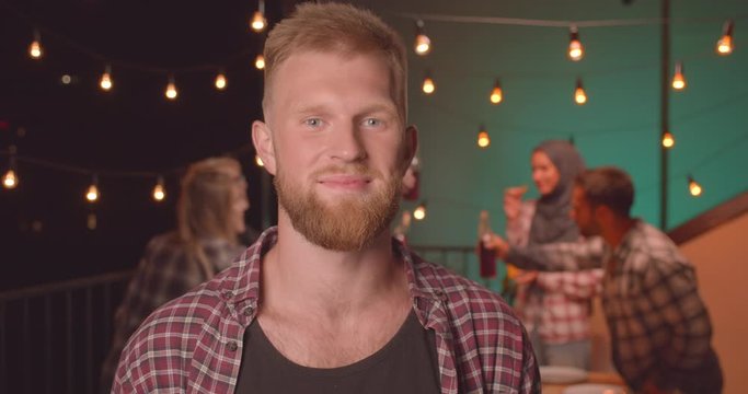 Closeup portrait of young redhead caucasian man at diverse party in cozy evening