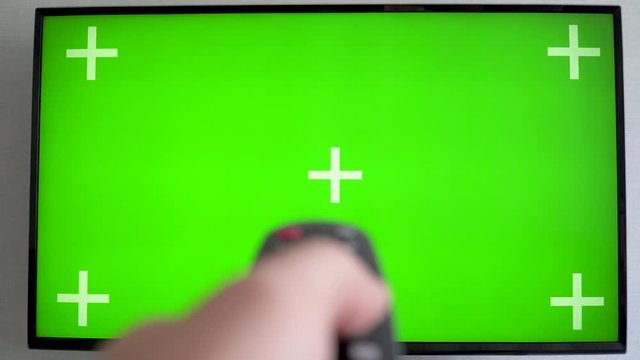 TV with green screen blurred TV Hand switches the channels by remote control Flat screen TV