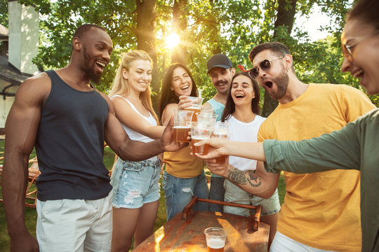 Group of happy friends having beer and barbecue party at sunny day. Resting together outdoor in a forest glade or backyard. Celebrating and relaxing, laughting. Summer lifestyle, friendship concept. - Powered by Adobe