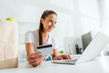 selective focus of happy girl holding credit card and using laptop