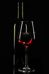 A glass and bottle of red wine and red grapes with reflaction on dark background