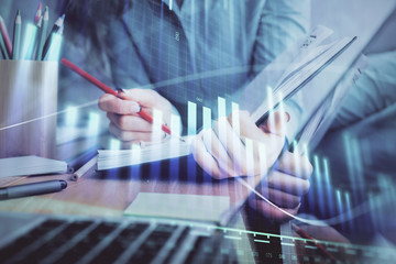 A woman hands writing information about stock market in notepad. Forex chart holograms in front....