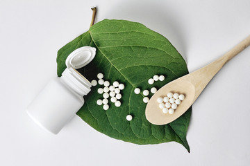 Homeopathy, naturopathy and alternative herbal medicine. Bottle with homeopathic pills on green...