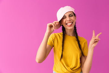 Obraz na płótnie Canvas Photo of brunette joyful woman wearing cap smiling and showing peace sign
