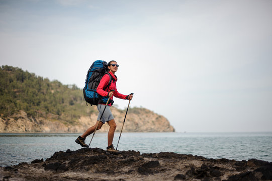 Woman in the sportwear walking on the rock on the sea with hiking backpack