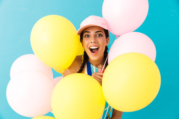 Image of happy surprised woman wearing cap looking at camera while holding air balloons