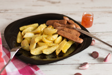 French fried potatoes on black plate with sauce on wooden table. Tasty french fries. Baked potatoes by slices.