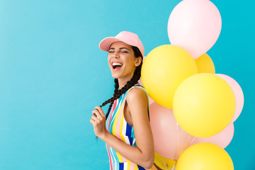 Image of young joyful woman wearing cap winking while holding air balloons