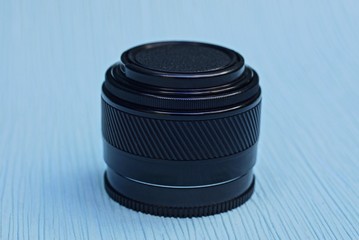 one camera lens closed by a black cap lies on a blue table