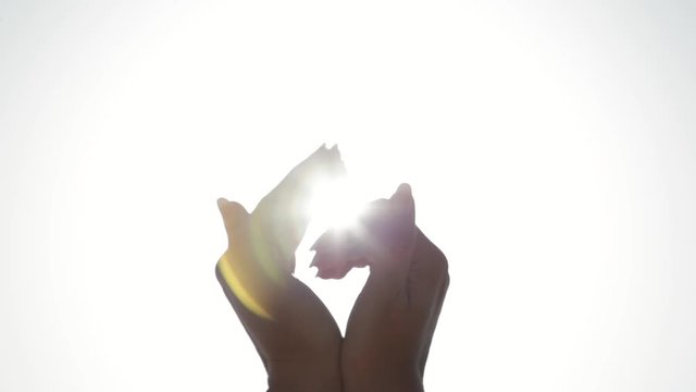 Closeup view of female hands with sun. Woman catching sunlight and making heart shape with fingers isolated at sunny early morning sunrise sky. Real time full hd video footage.
