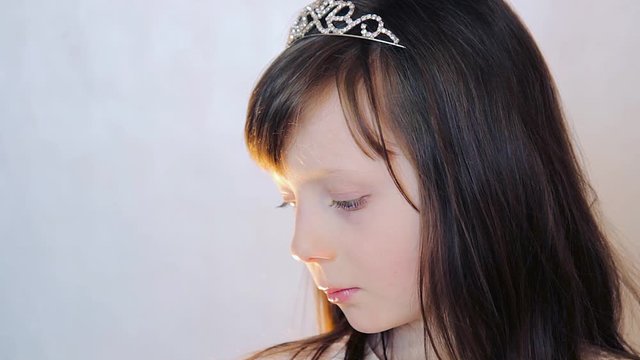 cute girl with princess crown and handheld fan looks into camera