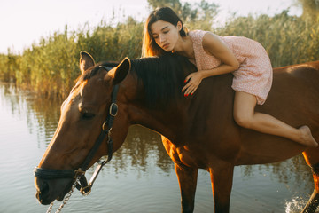 Woman lies astride a horse at river.
